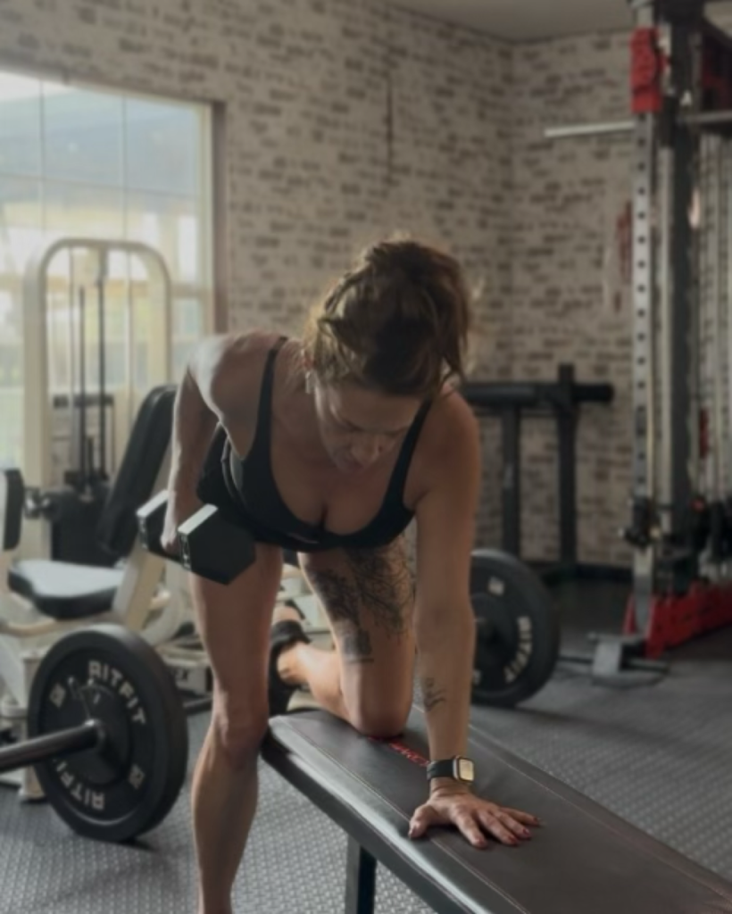 Woman doing a dumbbell row on a flat bench in a home gym